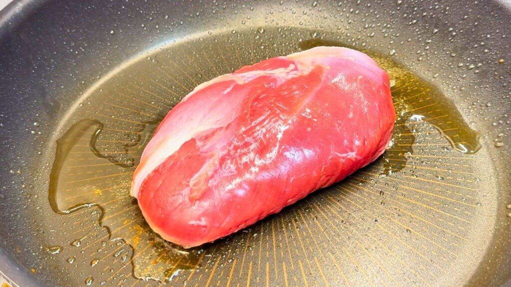Raw duck breast placed fat-side down in a preheated skillet, beginning the searing process to render the fat and create a crispy golden crust.