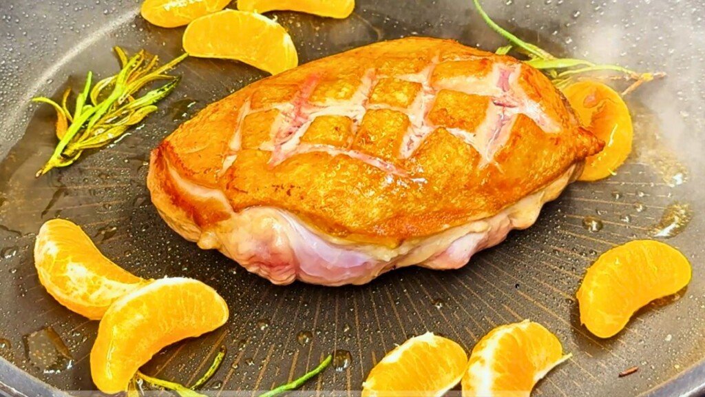 Pan-seared duck breast surrounded by fresh rosemary sprigs and juicy clementine wedges, cooking in a skillet before glazing.