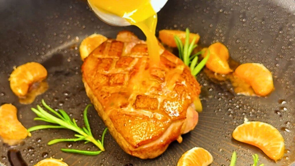 Honey orange glaze being poured over pan-seared duck breast, with rosemary and clementine slices in the pan for a flavorful citrus infusion.