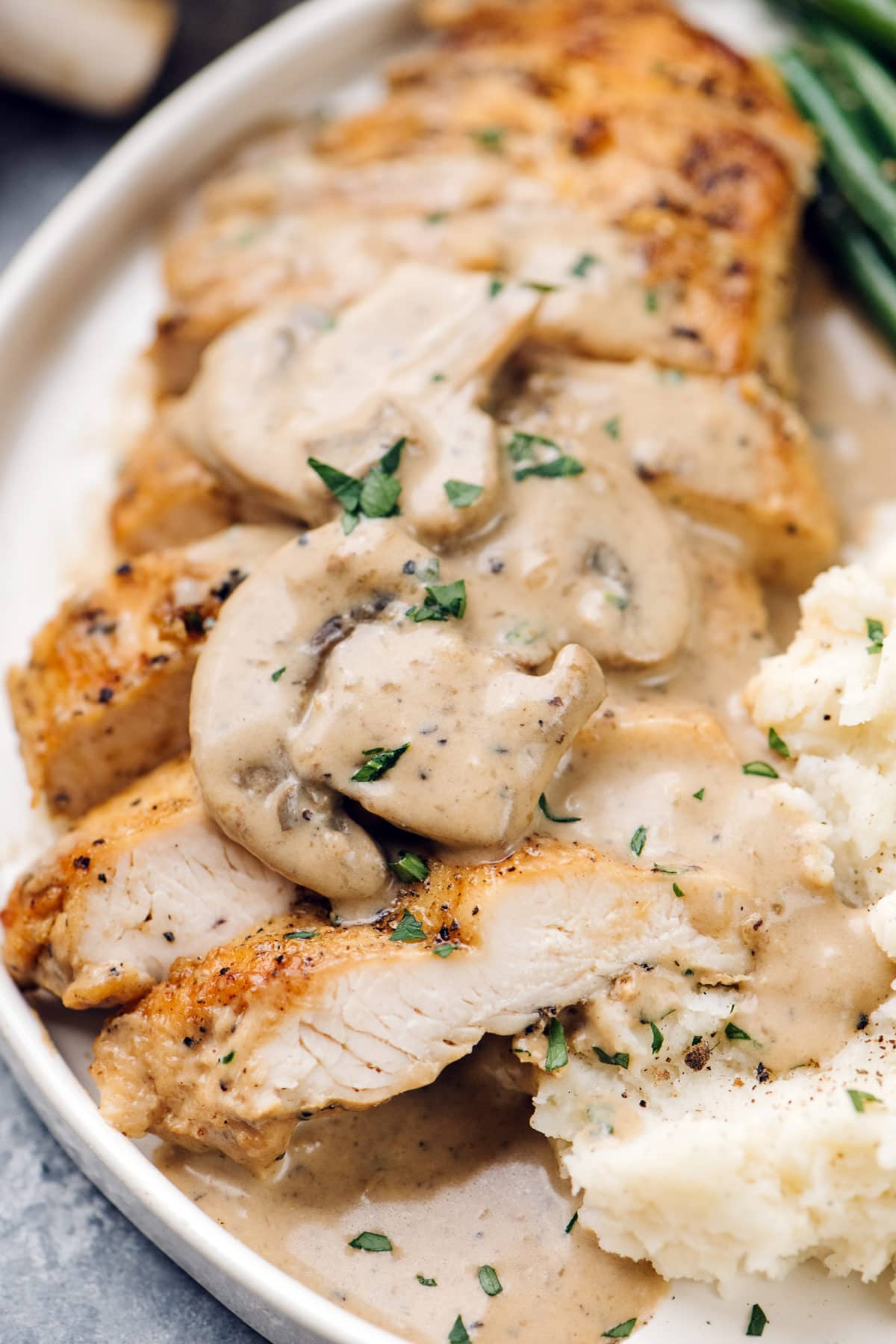 Pan-seared chicken breast slices topped with creamy mushroom sauce, served with mashed potatoes and garnished with fresh herbs.