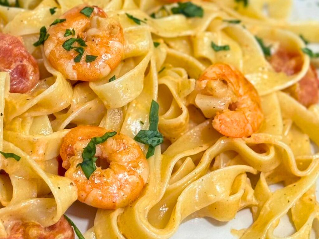 Close-up of creamy shrimp pasta with cherry tomatoes and garlic, garnished with fresh herbs