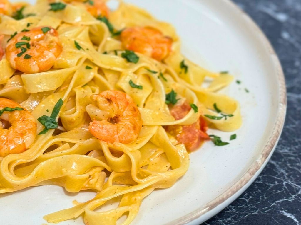 Plate of creamy shrimp pasta with tagliatelle, cherry tomatoes, and garlic cream sauce