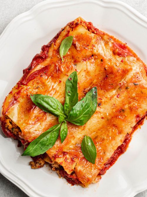 Baked mozzarella-stuffed cannelloni topped with golden cheese and fresh basil, served on a white plate.