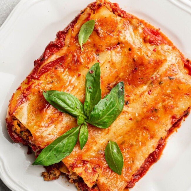 Baked mozzarella-stuffed cannelloni topped with golden cheese and fresh basil, served on a white plate.
