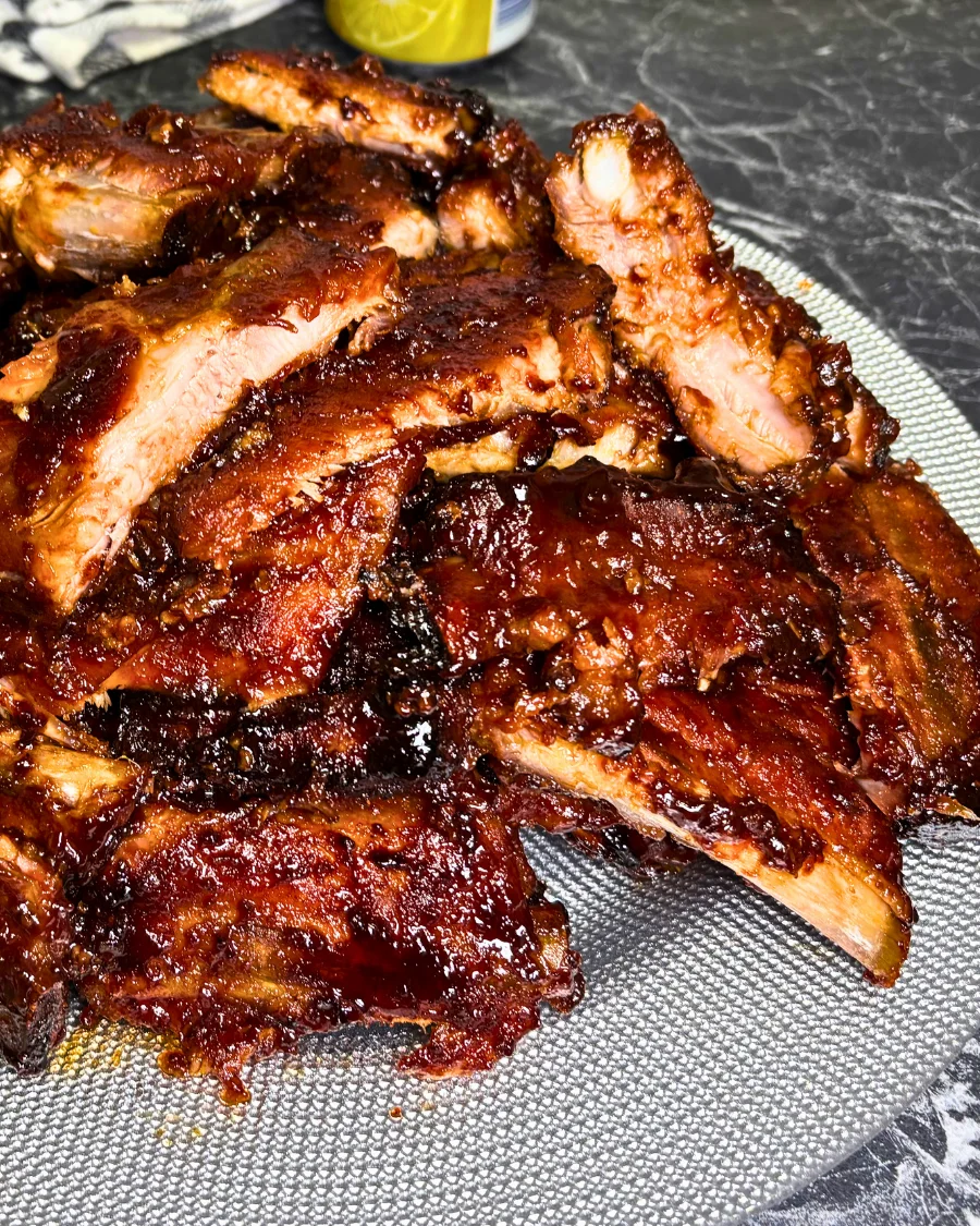 Sliced, glazed pork ribs arranged on a round serving platter, with a bowl of sauce in the background.