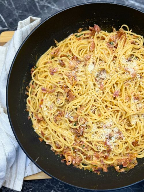 Creamy one-pot bacon pasta with spaghetti, crispy bacon bits, and grated Parmesan cheese served in a black skillet.
