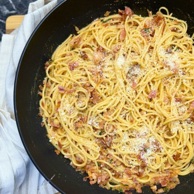 Creamy one-pot bacon pasta with spaghetti, crispy bacon bits, and grated Parmesan cheese served in a black skillet.