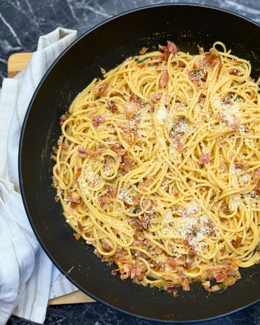 Creamy one-pot bacon pasta with spaghetti, crispy bacon bits, and grated Parmesan cheese served in a black skillet.