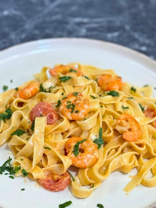 Close-up of creamy shrimp pasta with cherry tomatoes and garlic, garnished with fresh herbs