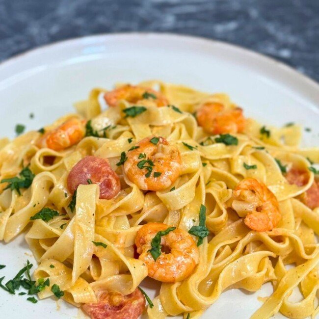 Close-up of creamy shrimp pasta with cherry tomatoes and garlic, garnished with fresh herbs