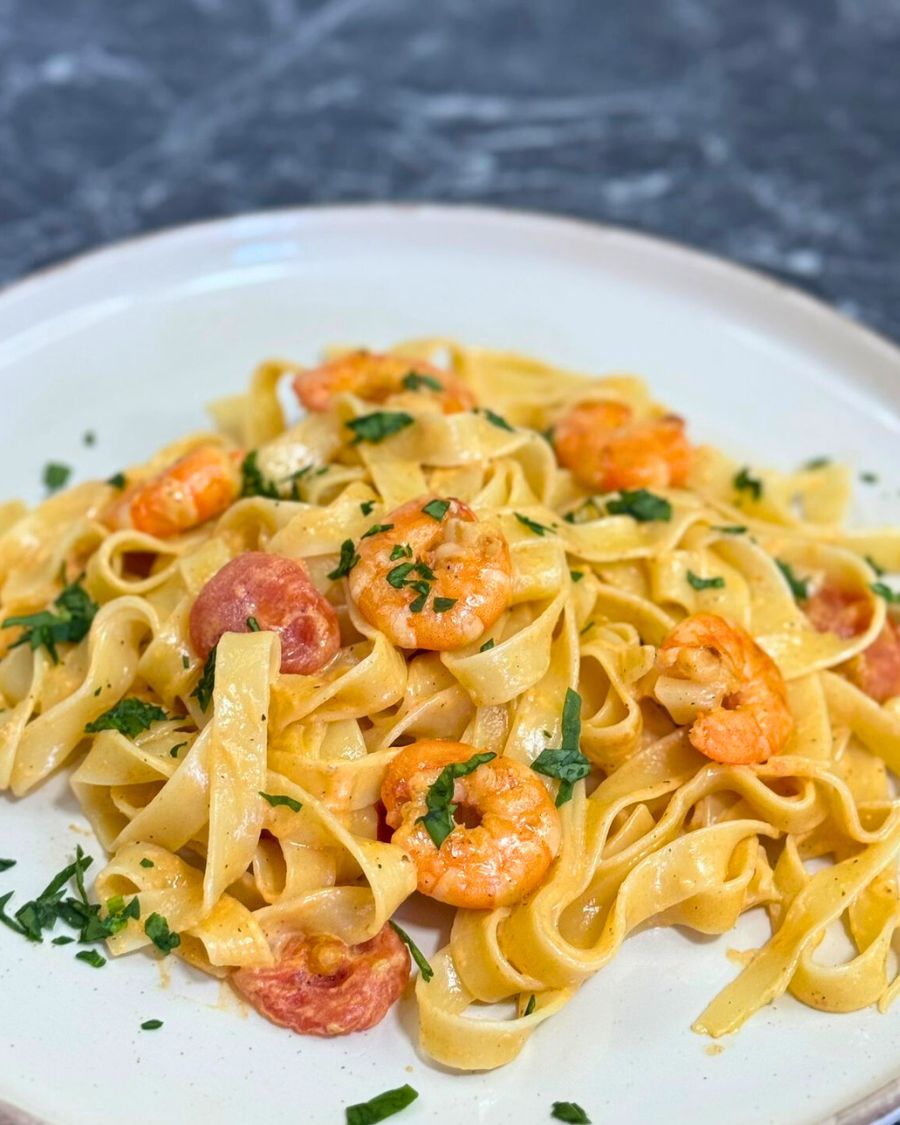 Close-up of creamy shrimp pasta with cherry tomatoes and garlic, garnished with fresh herbs