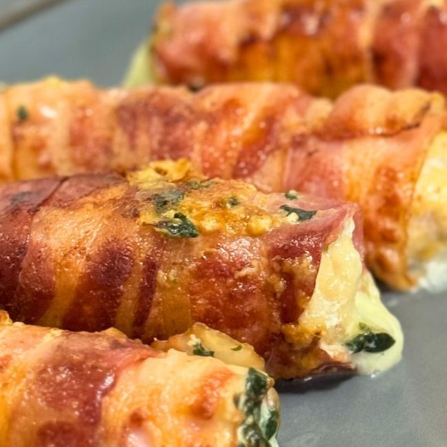 Bacon-wrapped chicken rolls stuffed with creamy spinach and cheese, cooked until golden and crispy.
