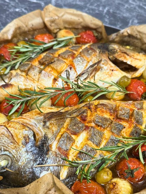 Two whole dorada fish baked with dark beer, cherry tomatoes, onions, olives, lemon, and fresh rosemary in a one-pot Mediterranean dish.