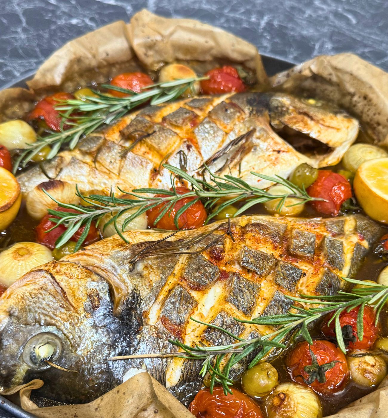 Two whole dorada fish baked with dark beer, cherry tomatoes, onions, olives, lemon, and fresh rosemary in a one-pot Mediterranean dish.