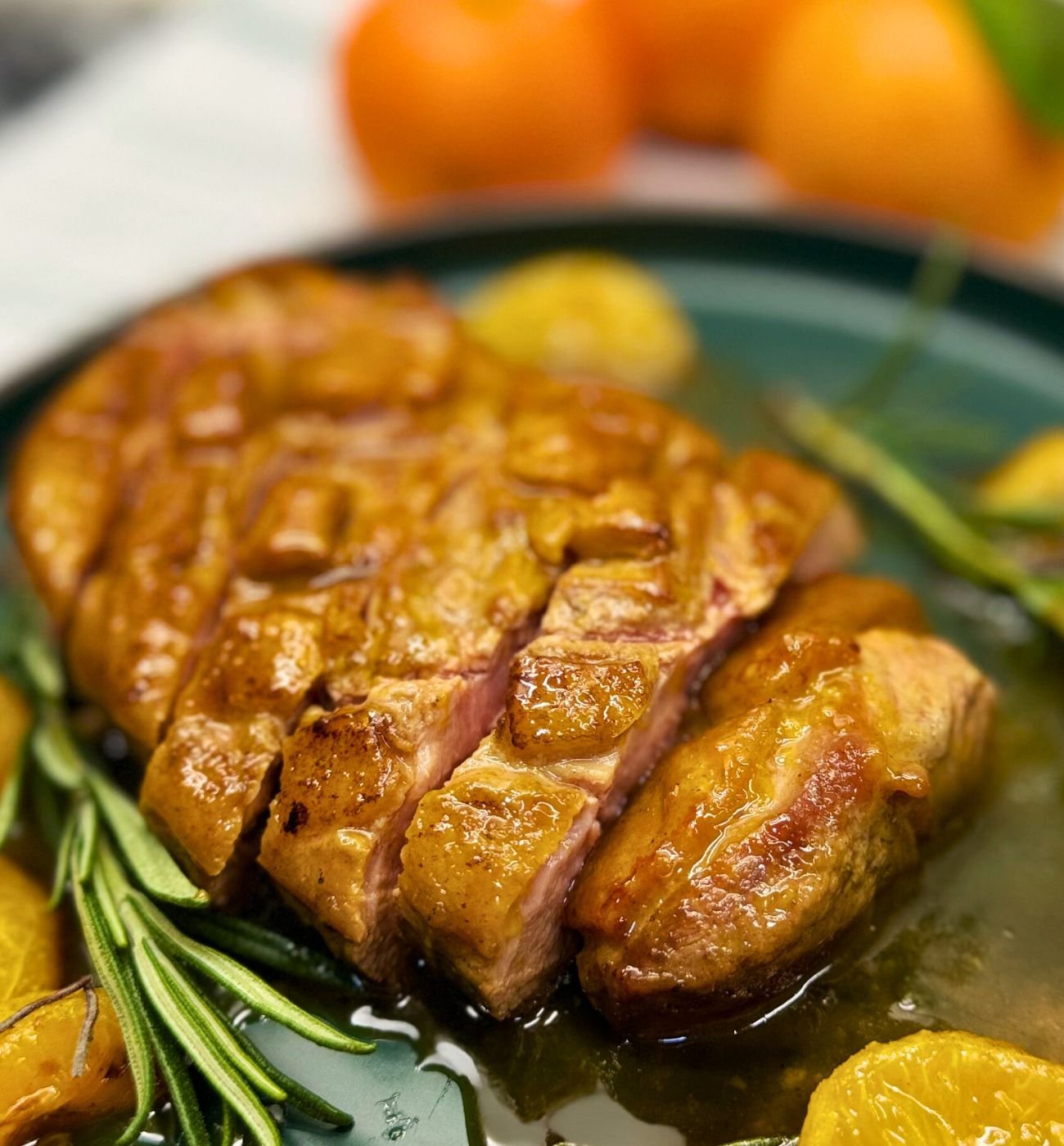 Close-up of sliced honey orange glazed duck breast with crispy golden skin and juicy pink center, served in citrus glaze with rosemary and clementines.