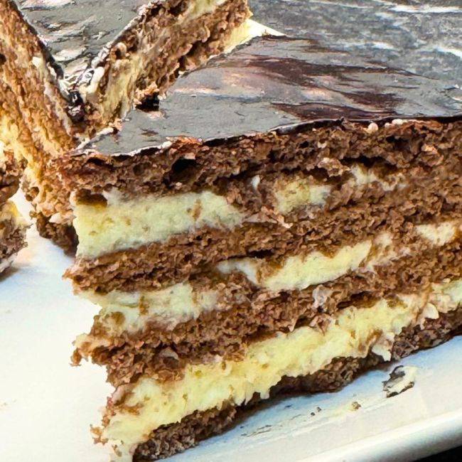 Layered Chocolate Spartak Cake with cocoa sponge, creamy custard filling, and glossy chocolate glaze cut into slices.