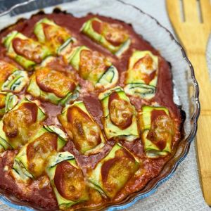 Freshly baked zucchini rollatini in a glass dish, with golden melted cheese and rich tomato sauce bubbling around the edges.