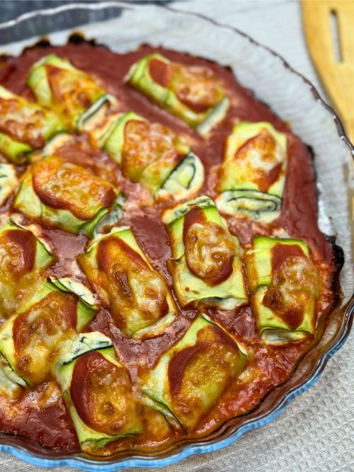 Freshly baked zucchini rollatini in a glass dish, with golden melted cheese and rich tomato sauce bubbling around the edges.
