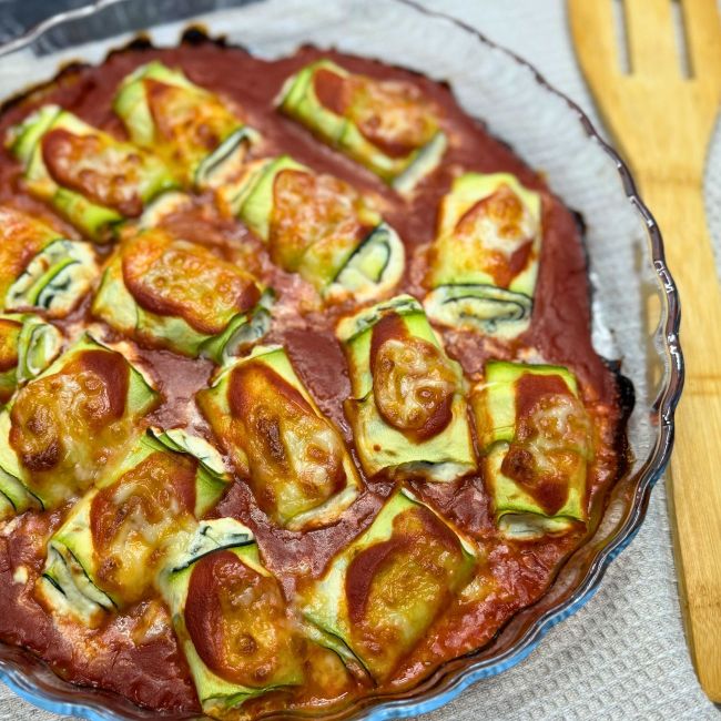 Freshly baked zucchini rollatini in a glass dish, with golden melted cheese and rich tomato sauce bubbling around the edges.