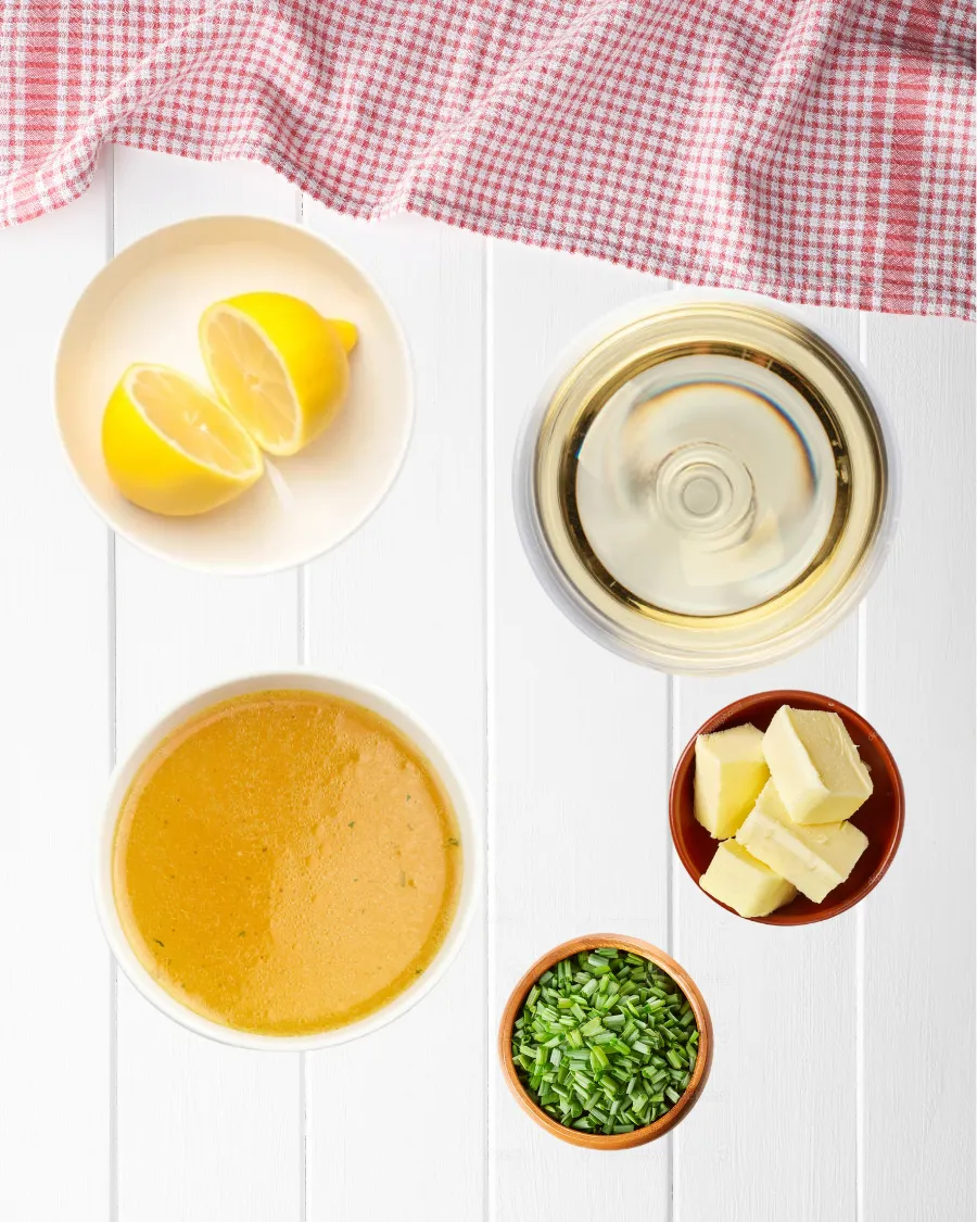 Top view of lemon butter sauce ingredients for chicken francese including lemon, white wine, chicken stock, butter cubes, and fresh chopped chives.