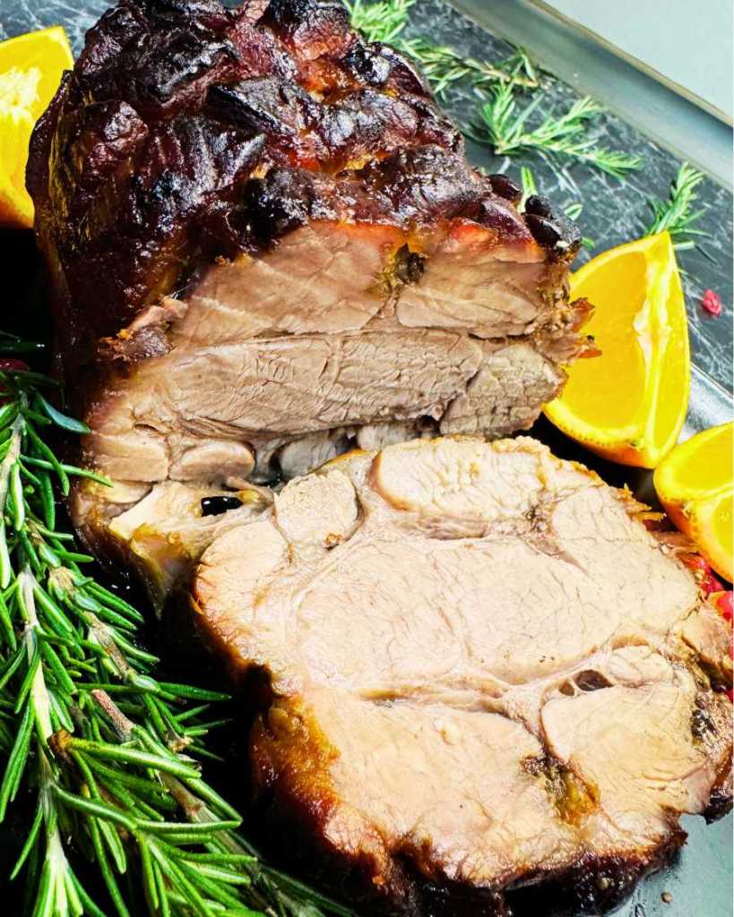 Juicy sliced oven roasted pork neck with caramelized honey soy glaze, served with orange slices and fresh rosemary