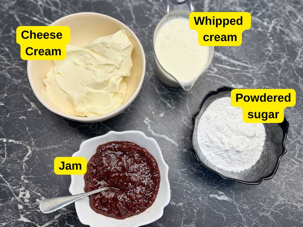 Four labeled ingredients for creamy pancake cake filling displayed on a dark marble countertop: a bowl of cream cheese, a jug of whipped cream, a black bowl of powdered sugar, and a white dish of raspberry jam with a spoon.