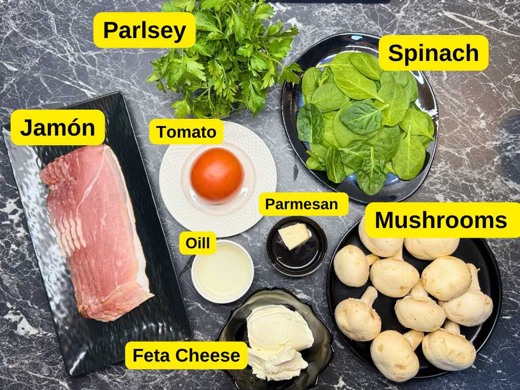 All ingredients for stuffed mushrooms displayed on a table, including mushrooms, feta cheese, jamón, spinach, parsley, tomato, Parmesan, and oil.