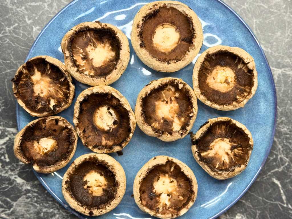 Cleaned mushroom caps with stems removed, arranged on a blue plate and ready to be filled for stuffed mushrooms.