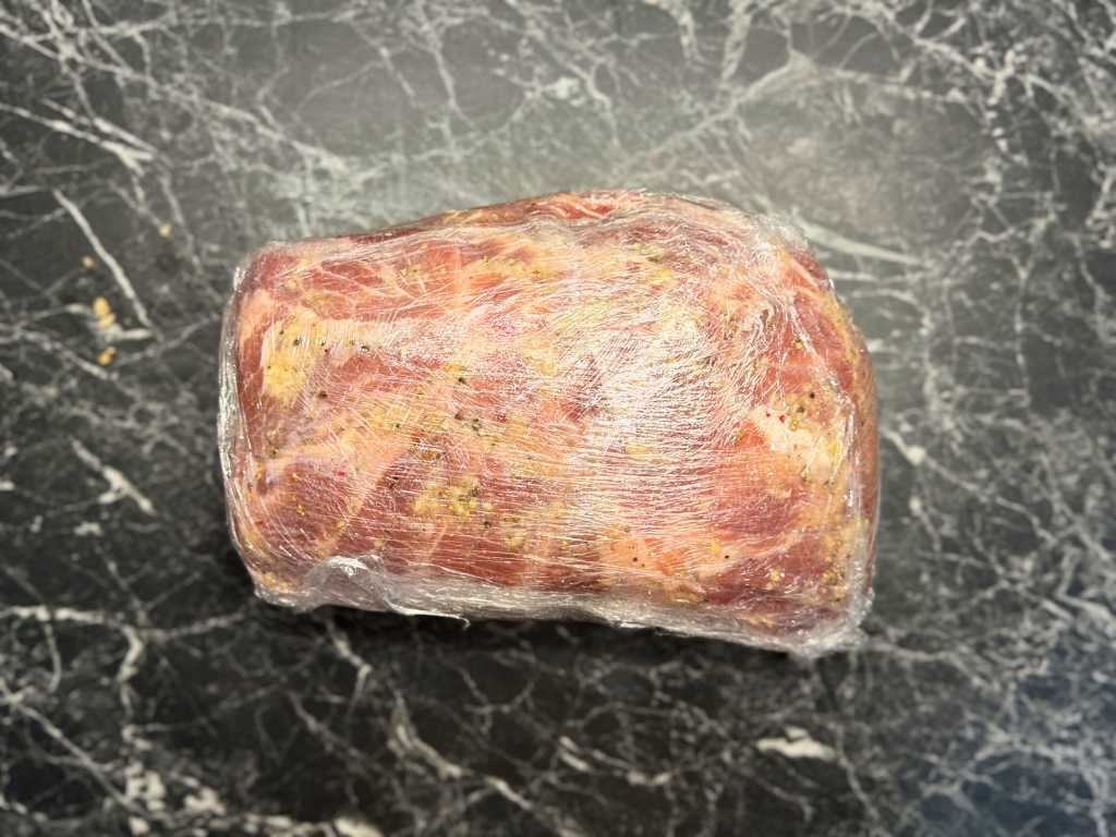 Seasoned pork neck tightly wrapped in plastic wrap for 24-hour marination