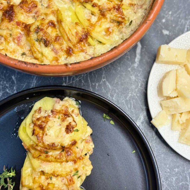 Creamy au gratin potatoes made with thinly sliced yellow potatoes, bacon, roasted garlic, heavy cream, and a blend of Gruyere, classic cheese, and Parmesan, baked until golden and bubbly