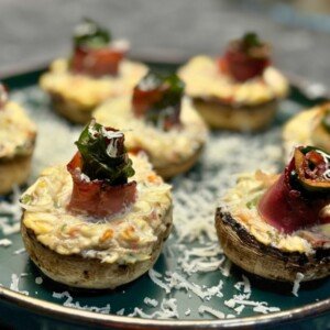 Baked stuffed mushrooms filled with creamy feta mixture and topped with jamón and spinach rolls, served with grated Parmesan.