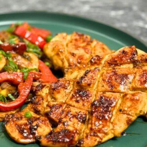 Asian-style chicken breasts scored and pan-seared until golden, served with sautéed bell peppers, mushrooms, and onions on a green plate.