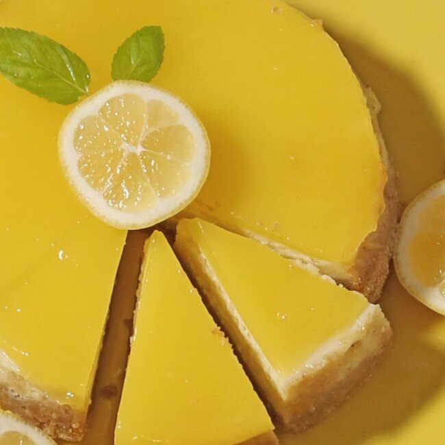 Slice of creamy lemon cheesecake garnished with fresh lemon zest and mint leaves.