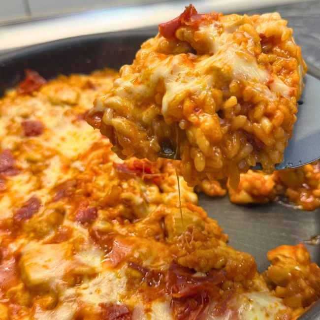One pan chicken and chorizo rice topped with melted cheese, being scooped from the pan.