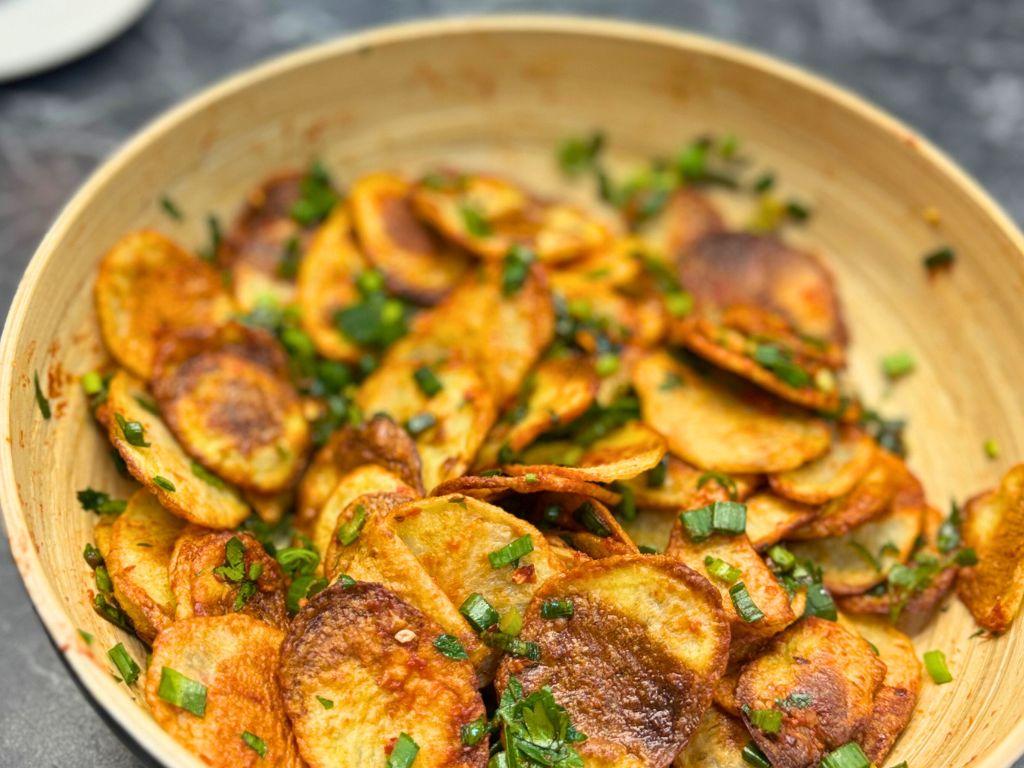 Bowl of crispy golden potato slices topped with fresh parsley and green onion.