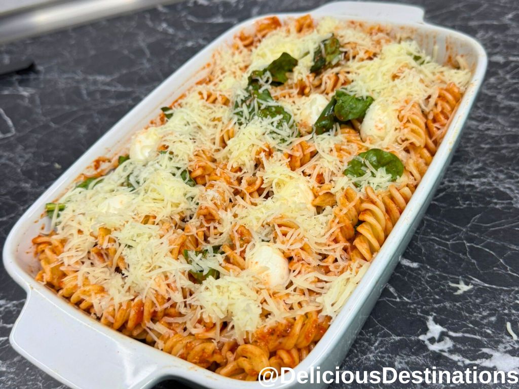 Baking dish with pasta, mozzarella and spinach leaves.