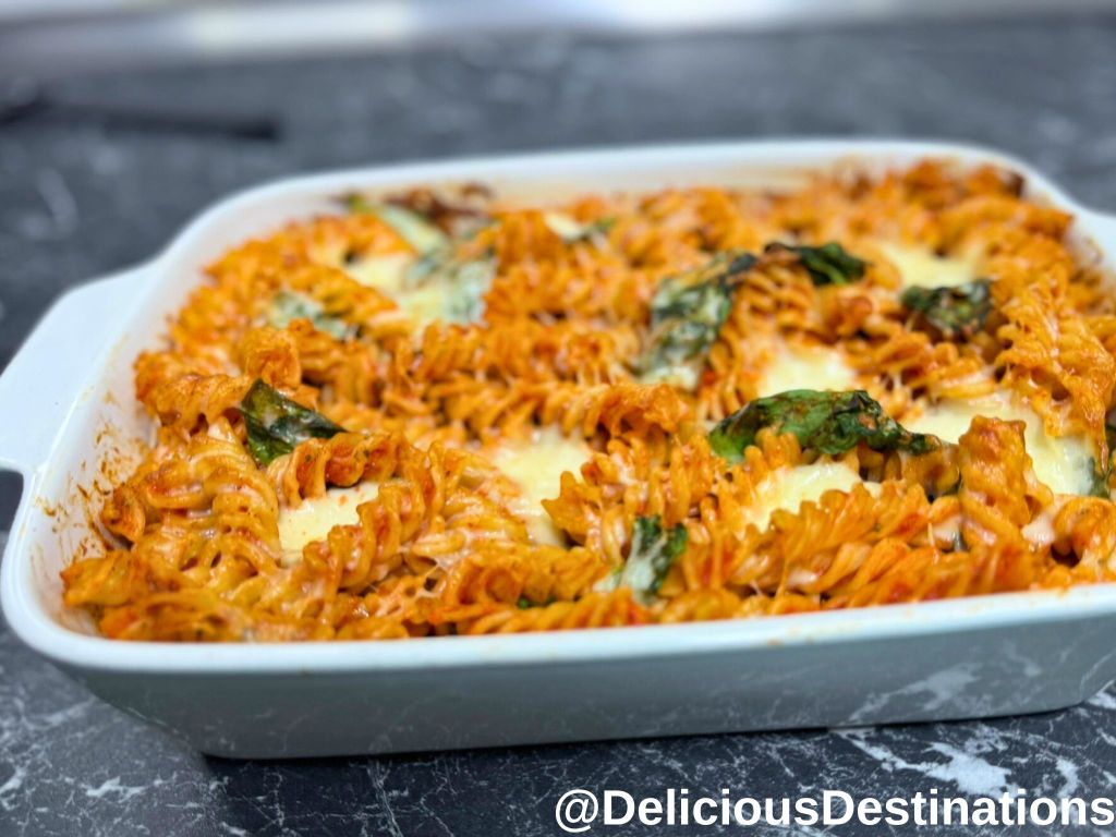 Baking dish with pasta, mozzarella and spinach leaves.