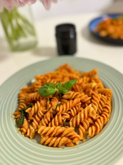 A plate of fusilli pasta with creamy roasted red pepper sauce, garnished with fresh basil.