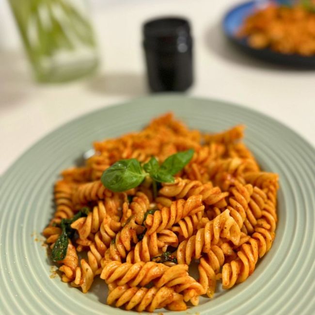 A plate of fusilli pasta with creamy roasted red pepper sauce, garnished with fresh basil.
