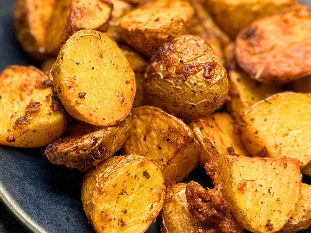 Close-up of crispy air fryer potatoes with golden edges, seasoned with garlic, herbs, and melted cheese, served on a dark plate.