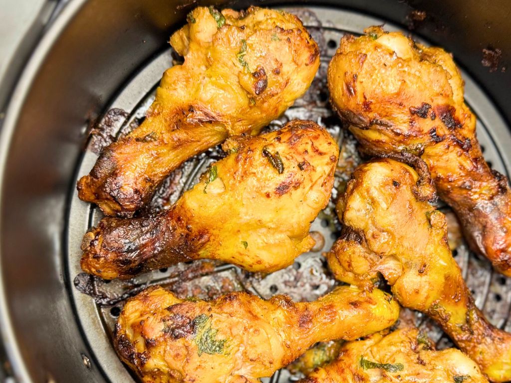 Golden brown mint-marinated chicken drumsticks cooking inside an air fryer basket, evenly crisped with visible herbs on the surface