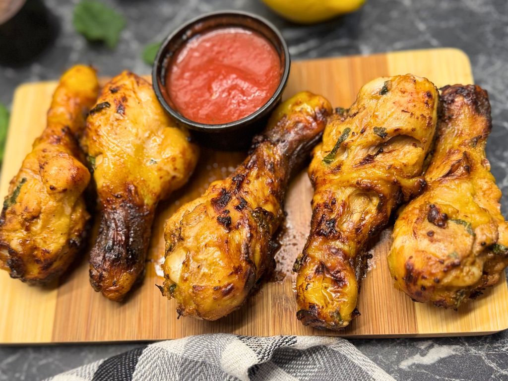 Crispy mint-marinated air fryer chicken drumsticks served on a wooden board with red dipping sauce, ready to enjoy