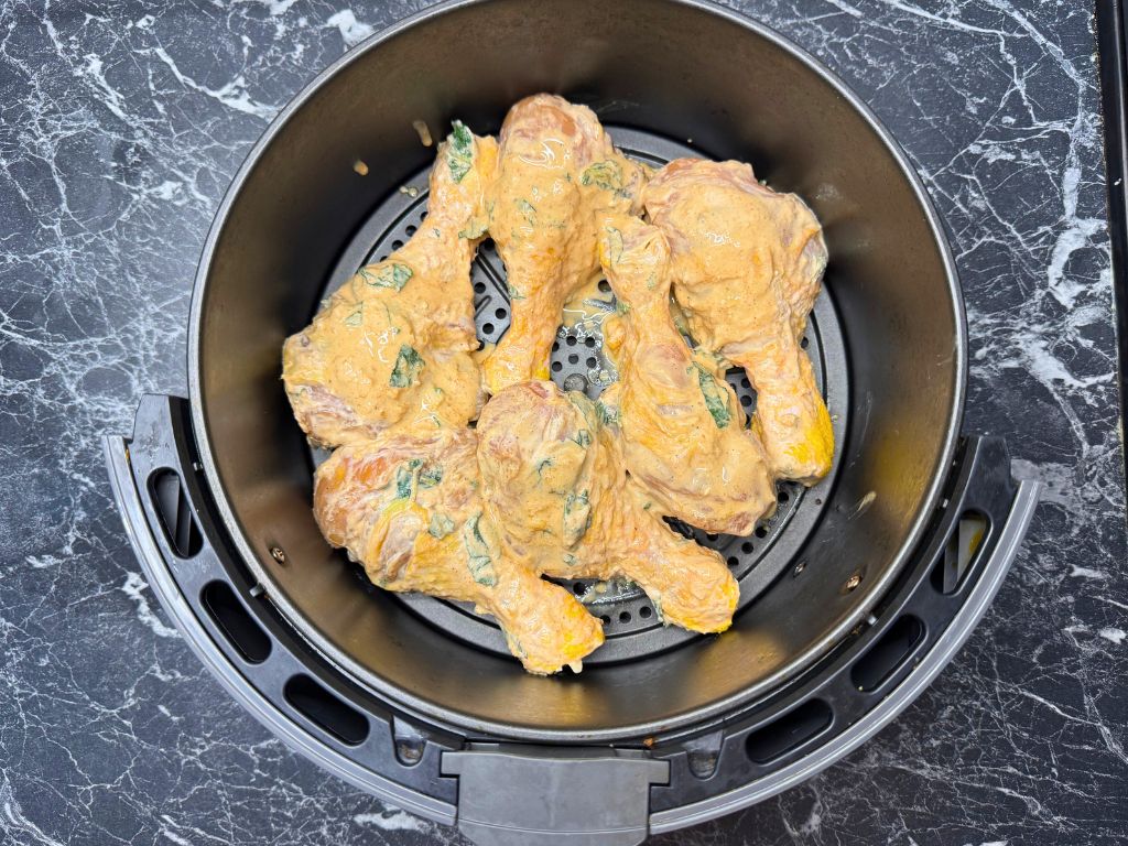 Marinated chicken drumsticks placed inside an air fryer basket, ready to cook with visible mint and creamy coating