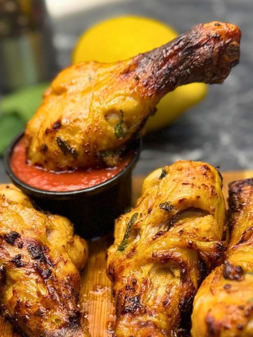 rispy air fryer chicken drumsticks with a mint marinade, served with a red dipping sauce on a wooden board