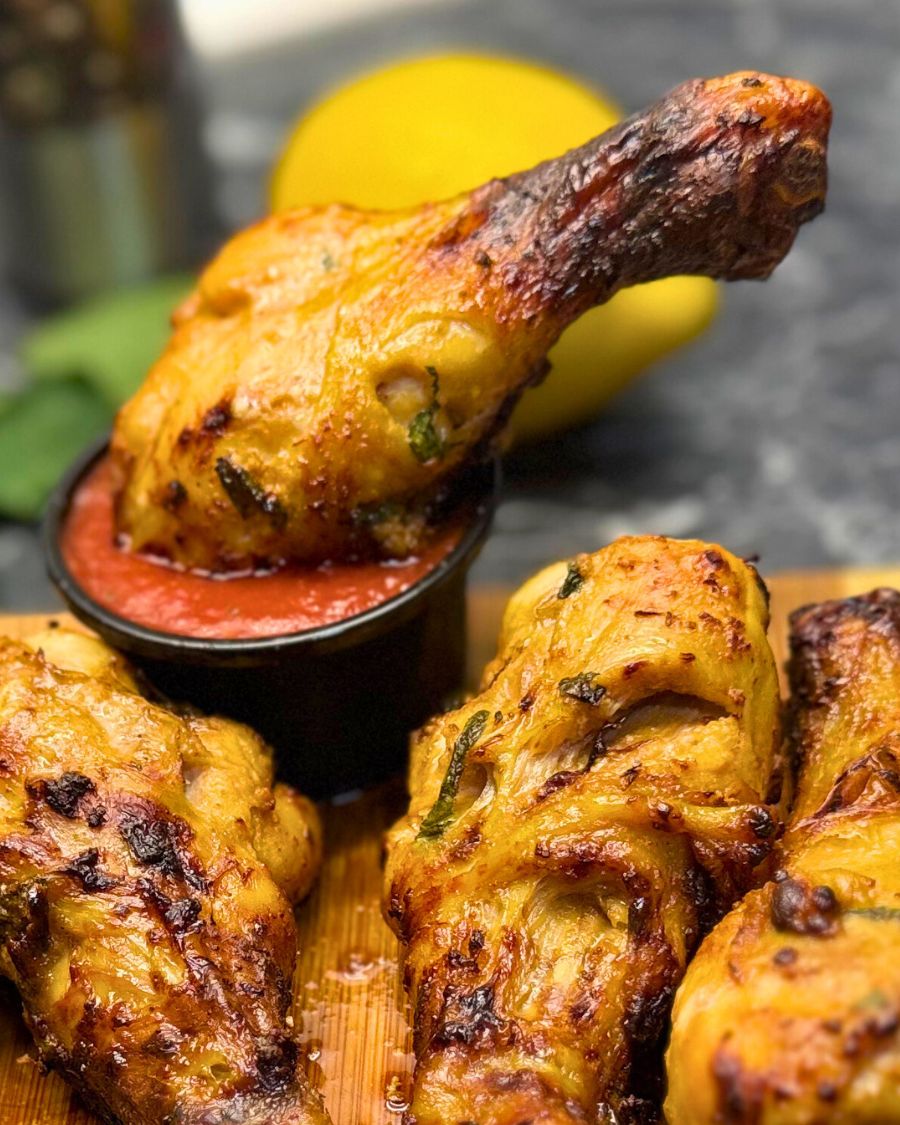 rispy air fryer chicken drumsticks with a mint marinade, served with a red dipping sauce on a wooden board