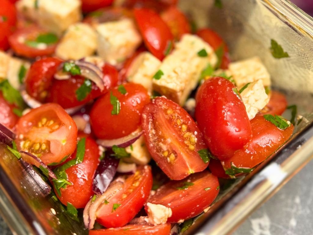Close-up of tomato feta salad showcasing glistening cherry tomato halves, fresh parsley, red onion slices, and creamy feta for a fresh summer dish.