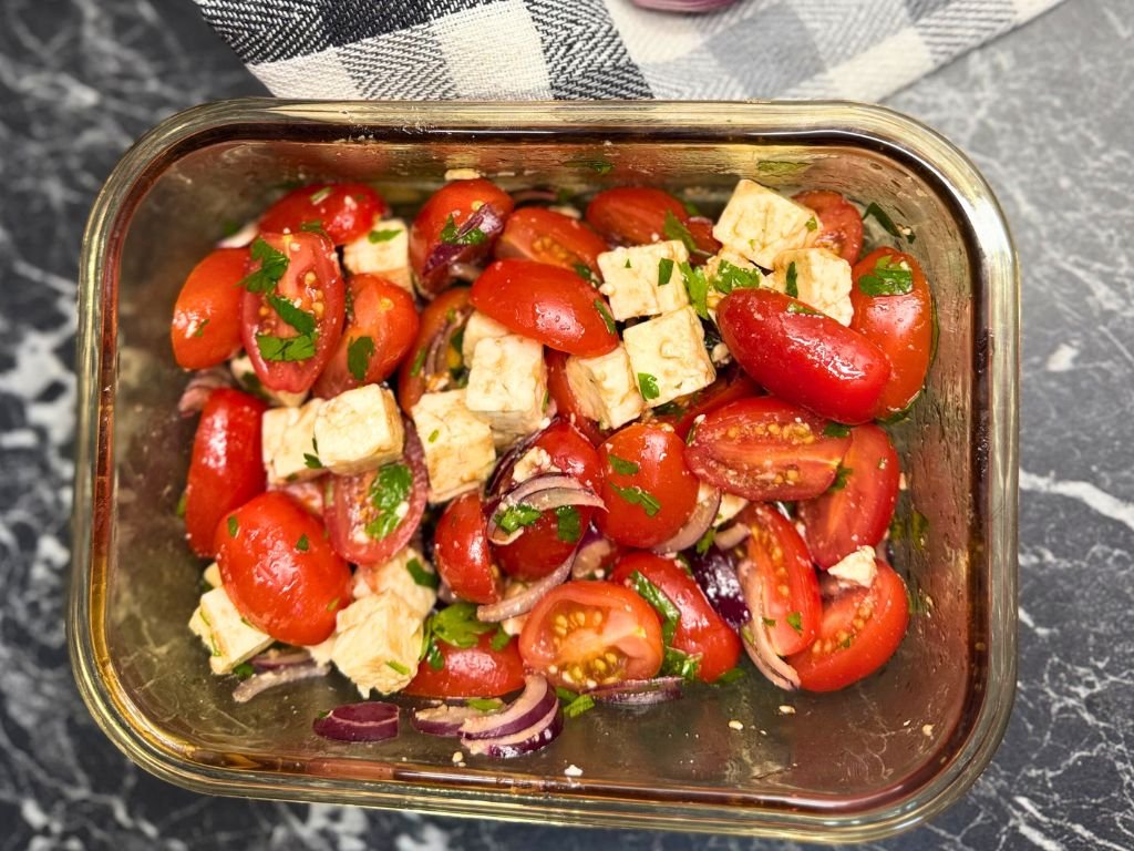 Overhead view of tomato feta salad in a glass dish, highlighting the vibrant red tomatoes, creamy feta cubes, and fresh green parsley.