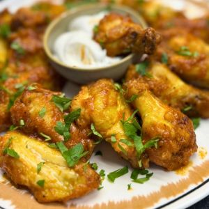Close-up of crispy air fryer chicken wings garnished with fresh parsley, served on a plate with a side of creamy dipping sauce.