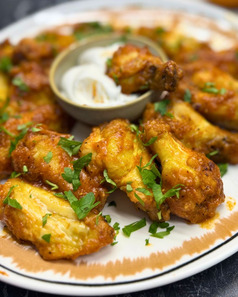Close-up of crispy air fryer chicken wings garnished with fresh parsley, served on a plate with a side of creamy dipping sauce.