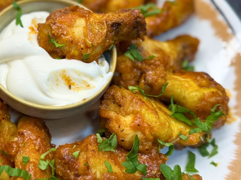 Extreme close-up of air fryer orange chicken wings with a crispy glaze, served with a creamy dipping sauce and topped with fresh parsley.